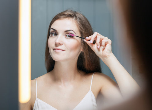 Woman applying mascara on long eyelashes in front of mirror