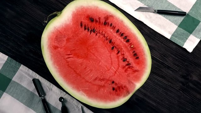 A half a red juicy ripe watermelon with set for carving rotation on the dark table, flat lay. Top view of water-melon, which ready for desserts. 4k