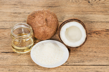Whole and half a coco next to a plate of coconut and a jar with oil on an old wooden table
