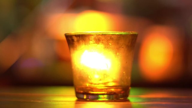 Candle in a glass stay on wooden table in blues music bar. Blurred backround. Bokeh. Colored illumination. 4K