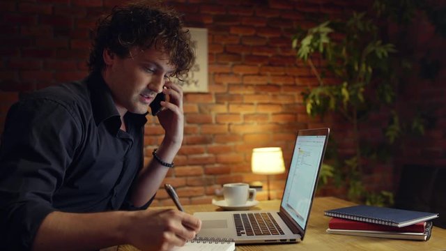 Young successful businessman smiling, speaking on phone, working in office at night.
