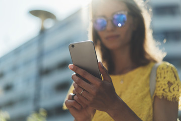 Close-up image of young smiling hipster girl using modern smartphone outside, beautifual woman...