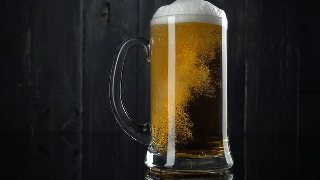 Slow motion shot of pouring beer into beer mug. Over dark wooden background
