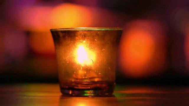 Candle in a glass stay on wooden table in blues music bar. Blurred backround. Bokeh. Colored illumination. Slow motion