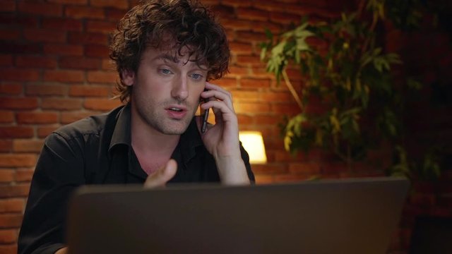 Young successful businessman speaking on phone, working in office at night. Slow motion.