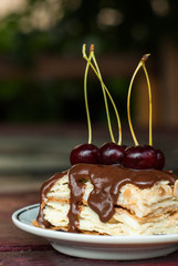 piece of cake with chocolate icing and cherries, puff pastry Napoleon  on a white plate,