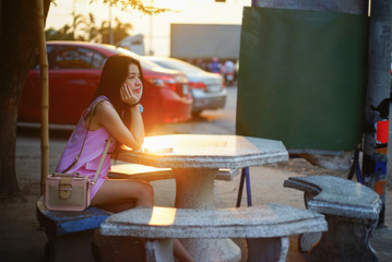 Portrait of young asian woman with little bag sitting on marble chair for waiting someone at sunset moment,filtered image,soft focus