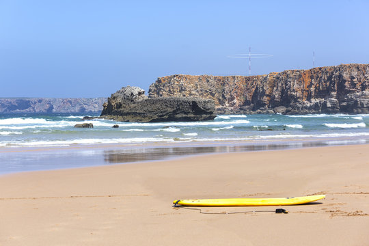 tabla de surf sobre la arena en una playa con olas , rocas y cielo azul