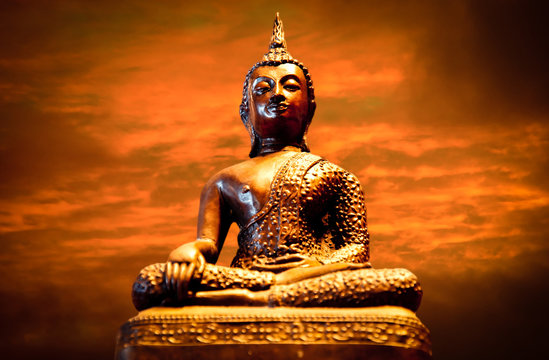 Photo of a statue of the Buddha meditating with sunset in the background