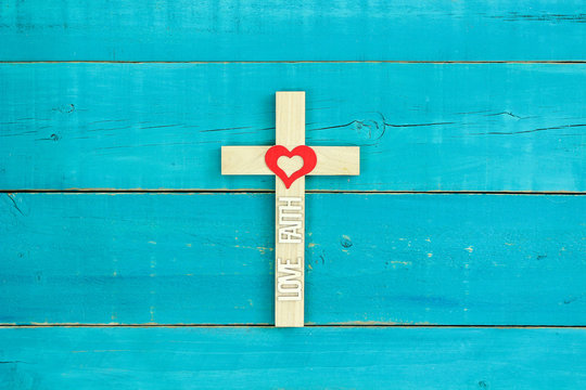 Wood cross with Love, Faith and red heart hanging on teal blue background