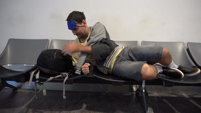 Man traveler backpacker trying to sleep at the airport on uncomfortable chairs
