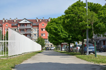 Residential building at the end of a pavement between white fence and street with trees