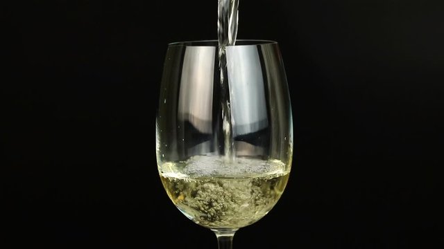 White wine pouring into glass on black background