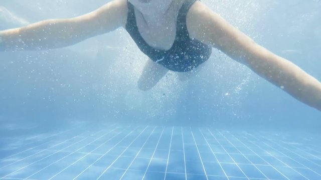 Joyful girl swimming underwater in pool. Slow motion.