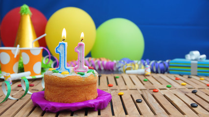 Birthday cake with candles on rustic wooden table with background of colorful balloons, gifts,...