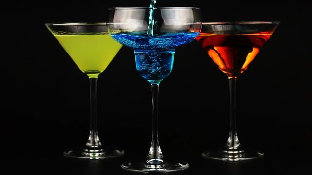 Pouring blue cocktail in wineglass. Three glasses of different cocktails edge on black background