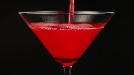 Pouring red cocktail in martini glass on black background - Powered by Adobe