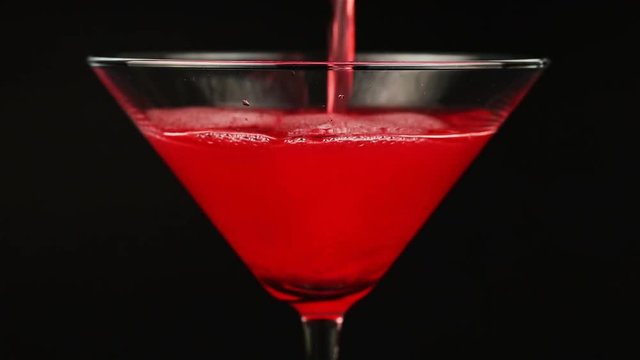 Pouring red cocktail in martini glass on black background