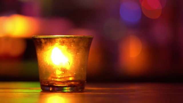 Candle in a glass stay on wooden table in blues music bar. Blurred backround. Bokeh. Colored illumination. 4K