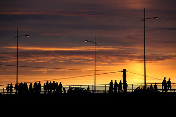 silhouettes of people and cars crossing the bridge at sunset, urban scene, vibrant colors