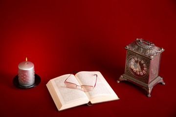 Clock, book and candle on red background