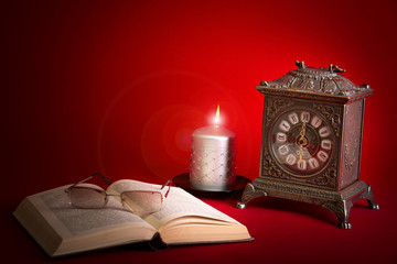 Clock, book and candle on red background