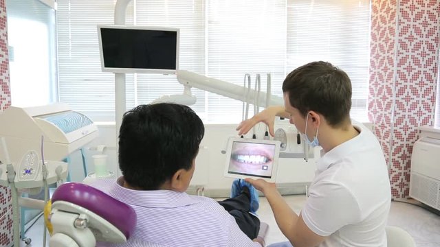 Dentist shows pictures of patient's teeth using a tablet with a touchscreen.