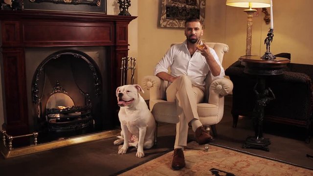 An aristocrat with a dog by the fireplace drinking whiskey.