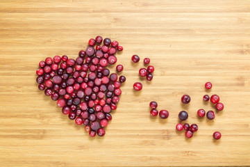 Cranberries in heart shape on wooden board with copy space, horizontal overhead view.