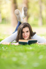 Beautiful girl lying on grass and relaxing with book