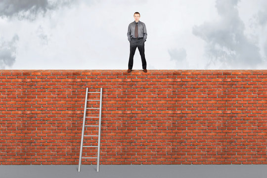 Assertive man stands on the top of a brick wall. Overcoming barr
