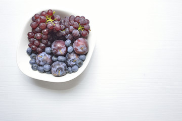 Purple and blue fruits on the withe dish on white wood.