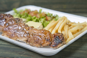 Fast food: kebabs, fries and fresh salad in the tray on the table. 