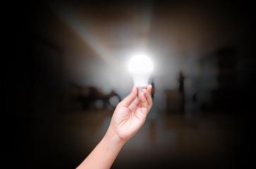 Woman hand hold lighting LED bulb on blurry indoor hall of offic