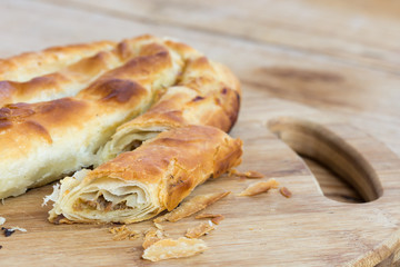 Sliced burek with meat on the wooden board. Rustic food.