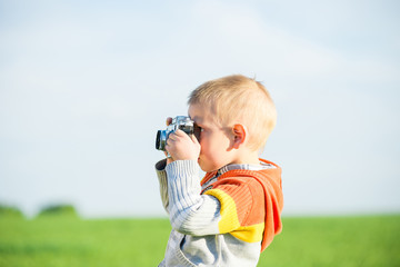 Little boy with an old camera shooting outdoor. Kid taking a photo using a vintage retro film cam. Green summer field.