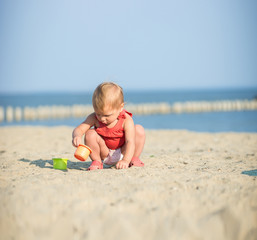 Baby playing on the sandy beach near the sea. Cute little girl in red dress with sand on tropical beach. Ocean coast.