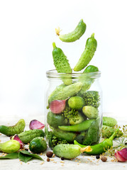 Cucumbers with herbs and spices for pickling in glass jar with flying ingredients on a white background.