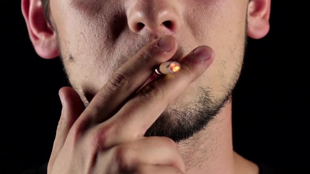 Man with a light beard smoking a long cigarette. Black. Close up. Slow motion