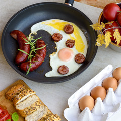 Fried sausages and eggs in a pan served with bread, tomatoes and egg shell, TOP VIEW
