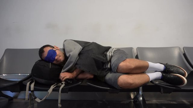 Man traveler backpacker trying to sleep at the airport on uncomfortable chairs