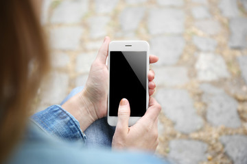Woman holding smartphone on blurred paving stone background