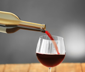 Red wine pouring in glass on grey background