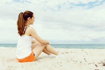 Fototapeta na wymiar Young woman in sports wear sitting at the beach