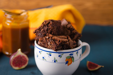 Brownie with walnuts, figs on a dark blue background with a yellow tablecloth in a white cup with blue flowers