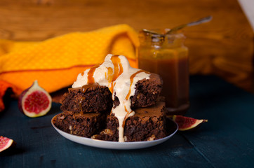 Brownie with walnuts, figs on a dark blue background with a yellow cloth with ice cream and salted caramel.