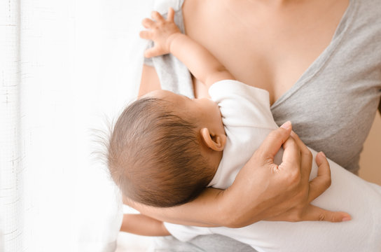 Mother breastfeeding her newborn baby beside window. Milk from mothers breast is a natural medicine to baby. Mother day bonding concept with newborn baby nursing.