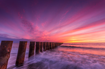 Fototapeta na wymiar Colorful sunset on Batlic sea beach with wooden groyne