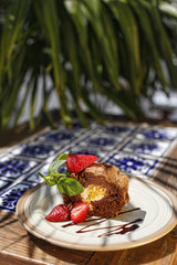 Chocolate Swiss-roll With Strawberries And Mint Leaves Basking In Sunshine With Palm Leaves In The Background 