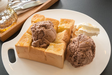 Honey toast served with chocolate ice cream and whipped cream on white dish. Interior shop.